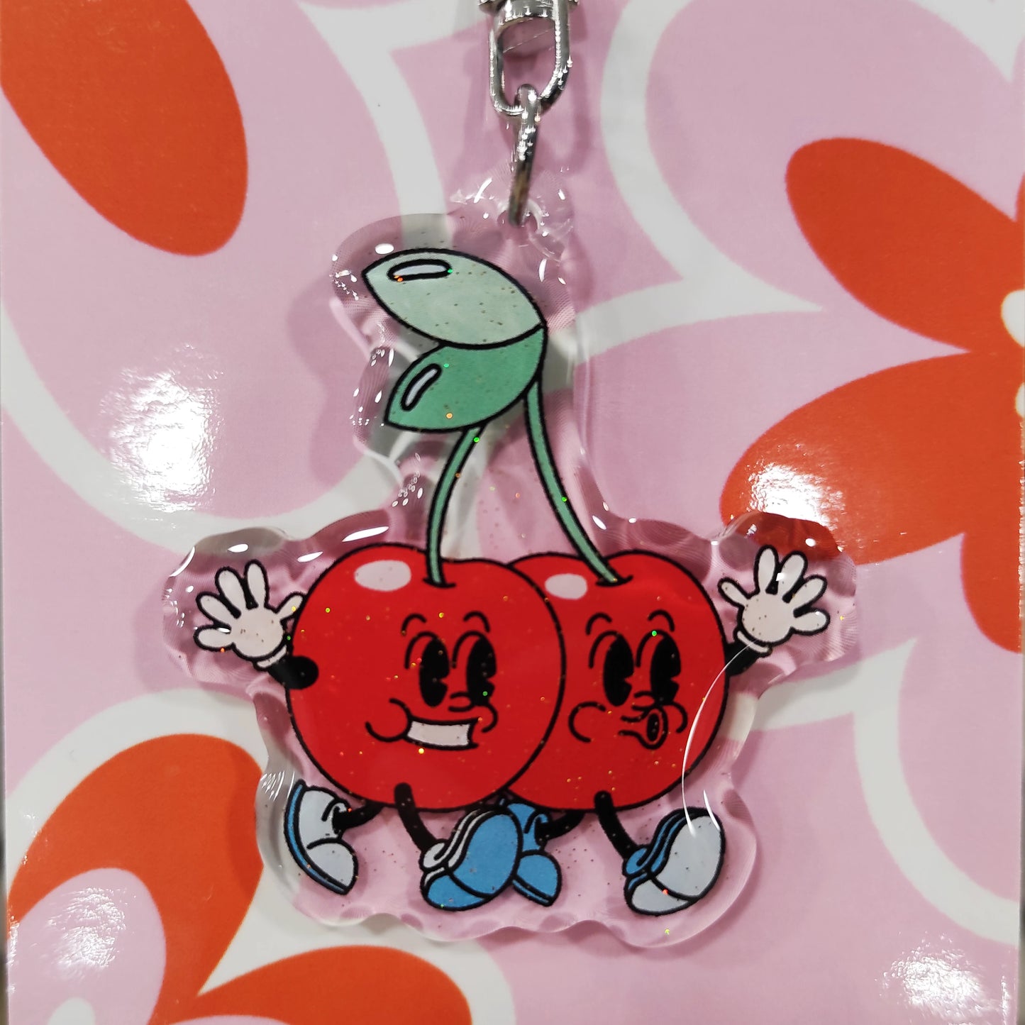 detalle del llavero con cerezas humanizadas de la artista Laura Ortiz, en material de resina con purpurina sobre fondo de cartón de flores