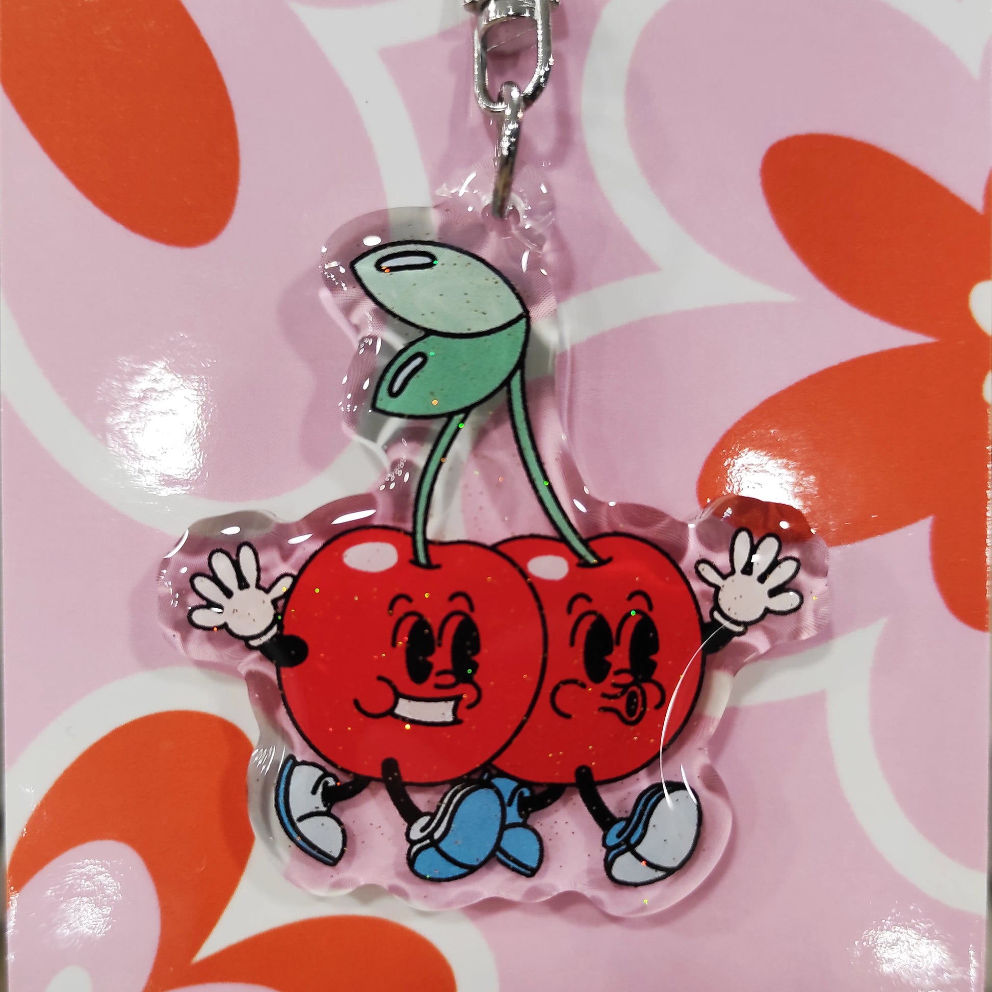 detalle del llavero con cerezas humanizadas de la artista Laura Ortiz, en material de resina con purpurina sobre fondo de cartón de flores