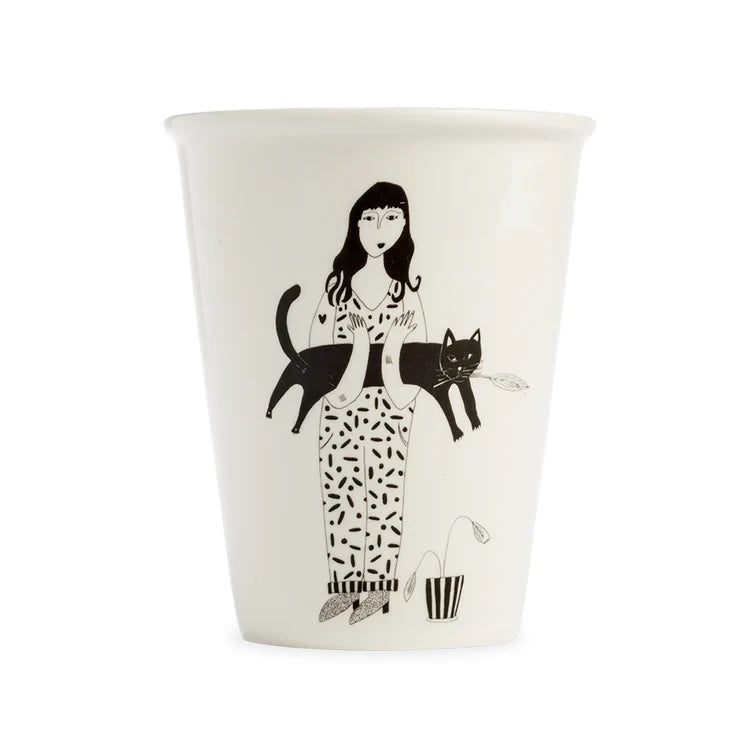 taza de porcelana con el dibujo en negro de una chica con el pelo largo con una planta a los pies y sujetando un gato negro