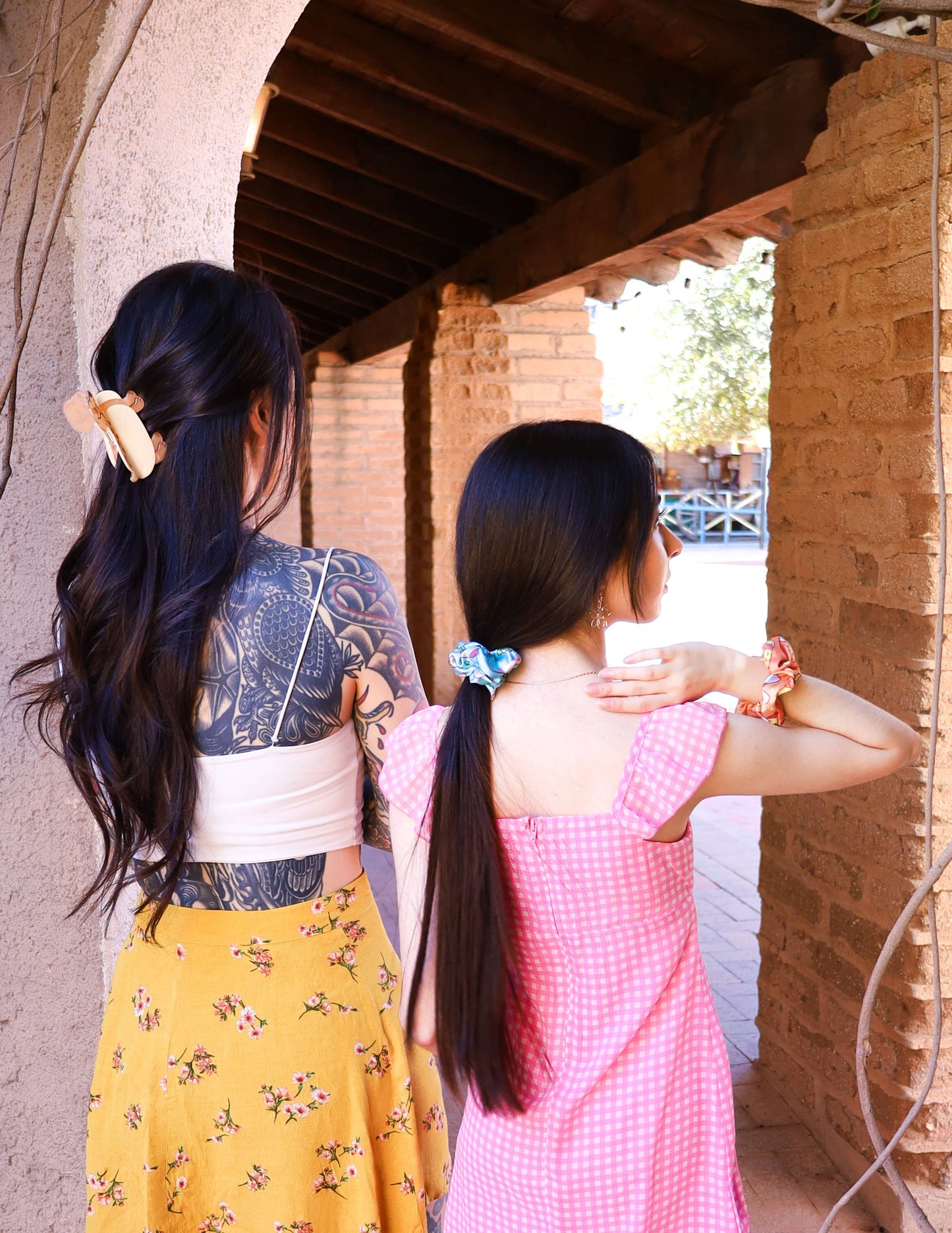 Dos chicas de pelo largo de espaldas, na con una coleta con un scrunchie y otra con una pinza de pelo con forma de perro salchicha