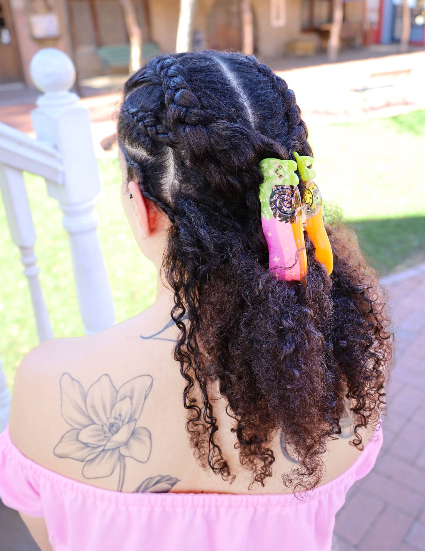 Chica de espaldas con trenzas sujetas con una pinza para el pelo de colores con forma de caracol dejando rastro de arcoiris
