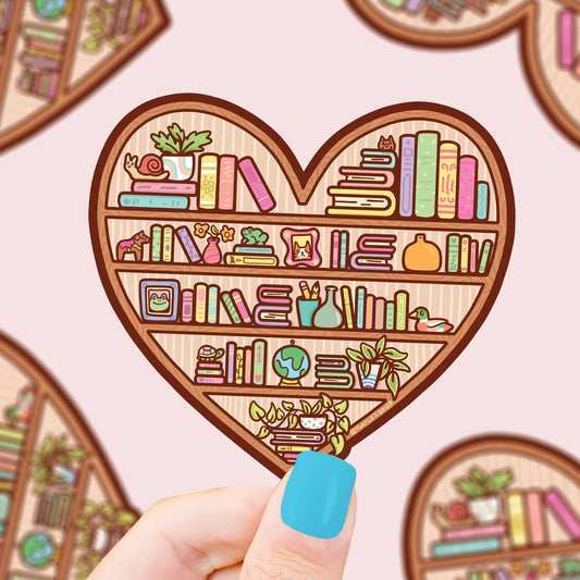 Pegatina con forma de corazón con una estantería llena de libros y objetos interesantes