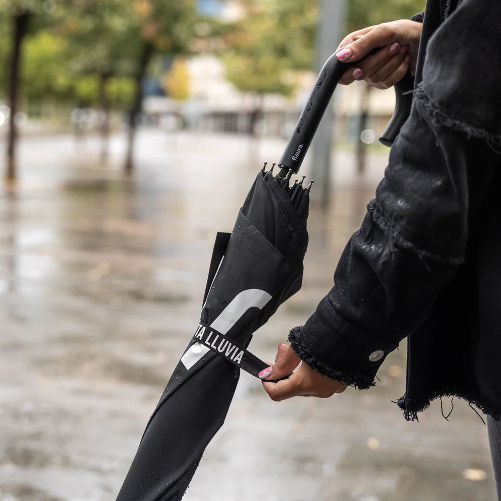 detalle del paraguas PUTA LLUVIA de Fisura cerrado con un mango en forma de gancho ergonómico y una tira que lo mantiene cerrado con el texto puta lluvia