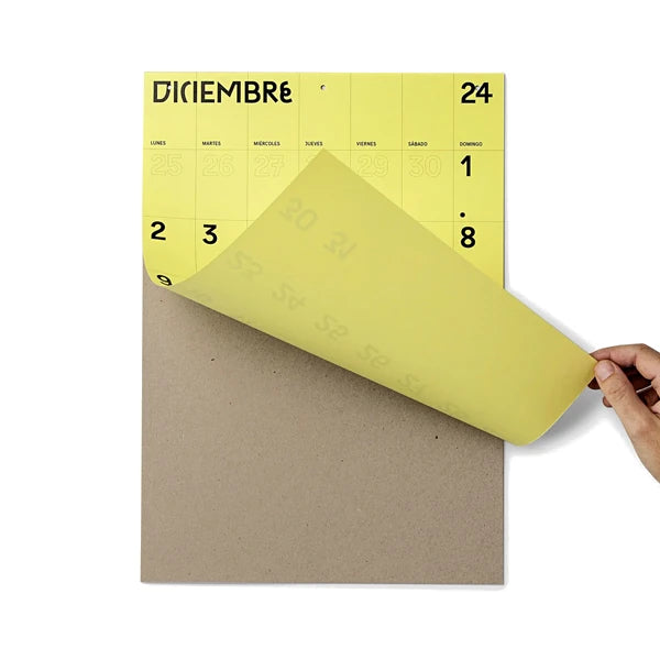 Mano levantando la página de diciembre del Calendario de pared 2024 a mes vista en papel amarillo tamaño A3 de Colla Paper