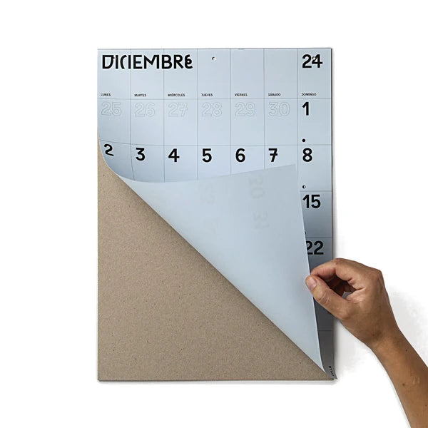 Mano levantando la hoja de diciembre, la última del calendario de pared 2024 en papel azul y tamaño A3 de Colla Paper