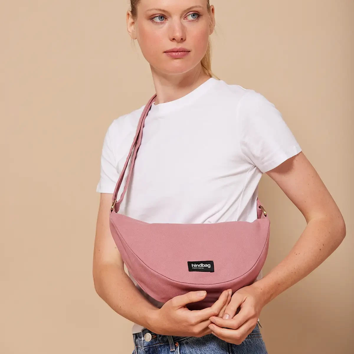 Mujer con camiseta blanca y el bolso riñonera rosa de la marca Hindbag con forma de media luna