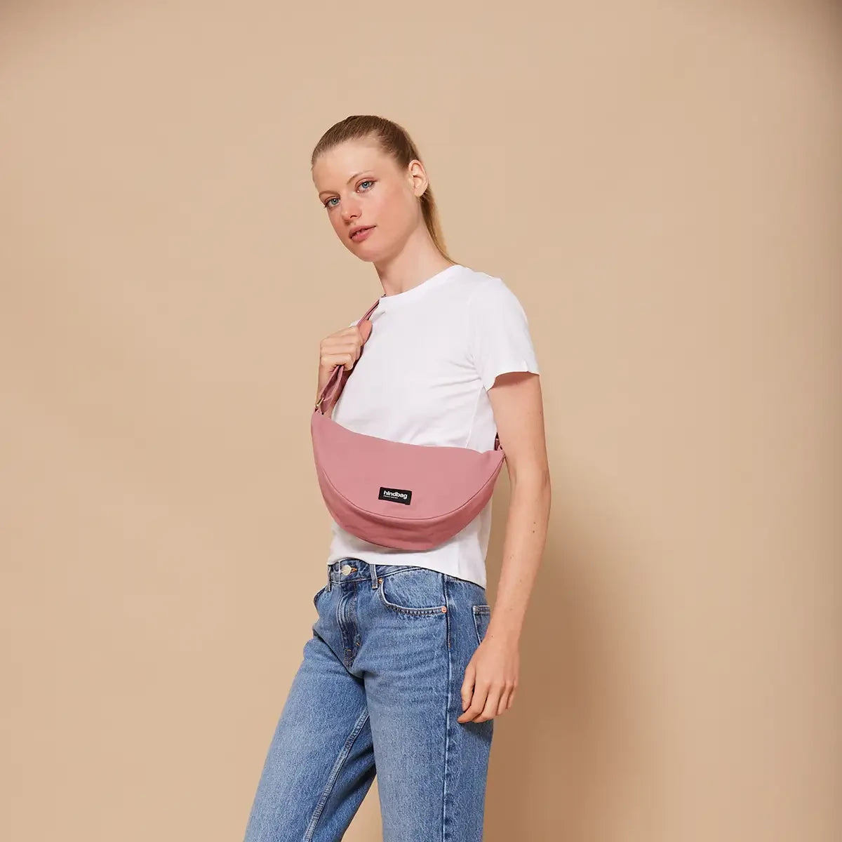 Mujer con camiseta blanca y el bolso riñonera rosa de la marca Hindbag con forma de media luna