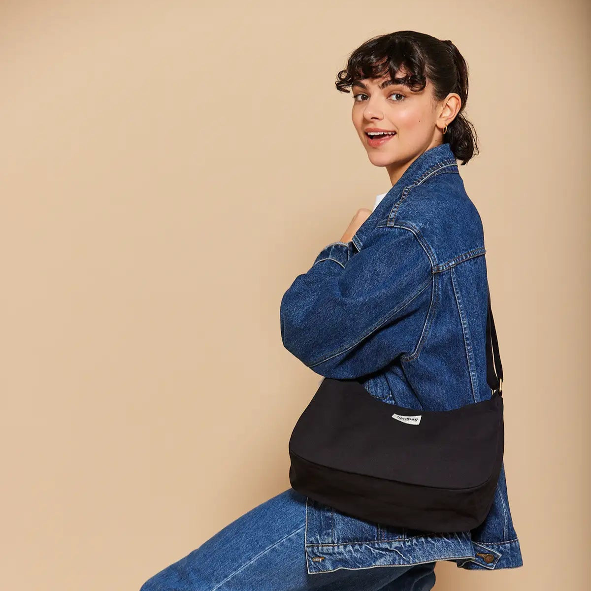Mujer vestida de vaquero con bolso de bandolera en color negro hecho de algodón orgánico de la marca francesa Hindbag