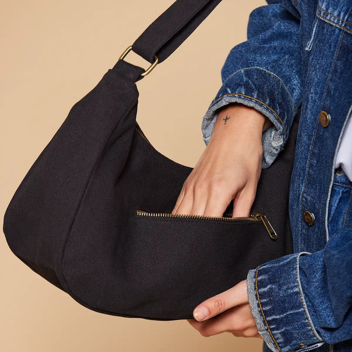 Mujer metiendo la mano en el bolsillo trasero del bolso de bandolera u hombro en color negro hecho de algodón orgánico de la marca francesa Hindbag