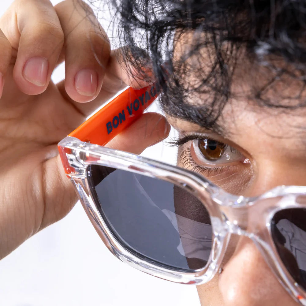 detalle de las gafas de sol de Fisura del modelo Bon Voyage cuadradas con la parte delantera transparente y los cristales en negro y en interior de la patilla roja con el texto "BON VOYAGE" en negro