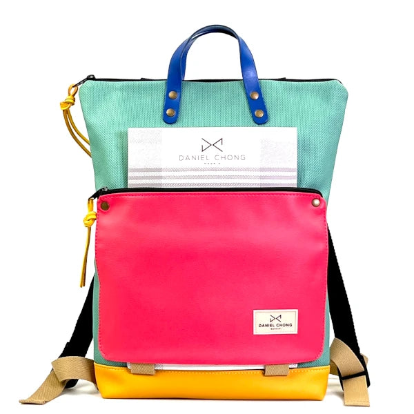 Mochila Book Holder de Daniel Chong con cuerpo impermeable de color turquesa y bolsillo delantero con cremallera de piel rosa