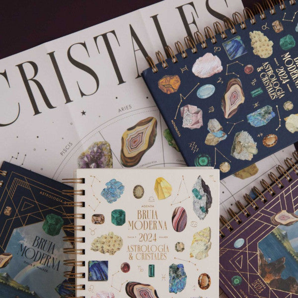 Varias agendas de la Bruja Moderna para 2024 sobre el póster desplegable con los cristales correspondientes a cada signo del zodiaco