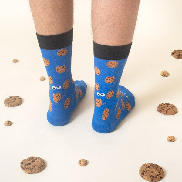 Piernas con los calcetines del color del Monstruo de las Galletas estampados con galletas con pepitas de chocolate y el mensaje Eres muy cookie en un suelo cubierto de galletas con pepitas de chocolate