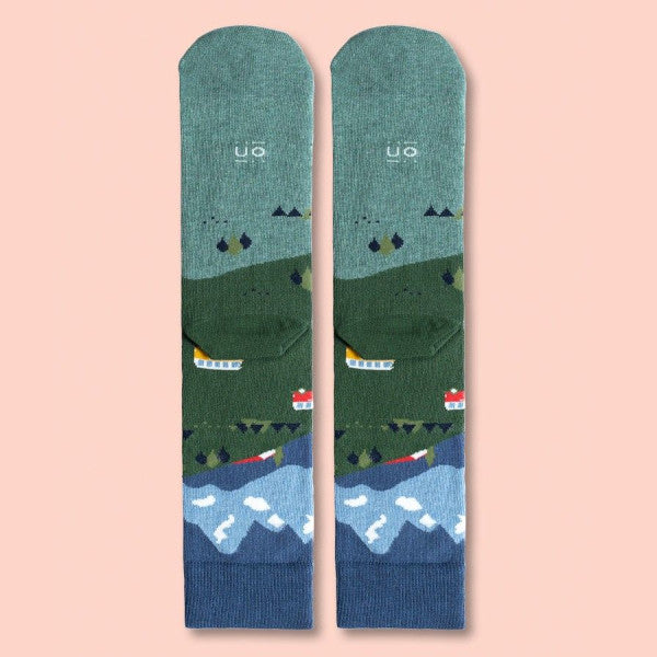 Parte de atrás de los calcetines con estampado de montañas tiendas de campaña, una camper y el globo del mundo y el mensaje Que te quiten lo viajao