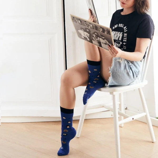 Mujer sentada en una silla blanca mirando discos de vinilo con los calcetines azules con el mensaje Eres un temazo y estampado de rayos, notas musicales y caras de iconos de la música puestos