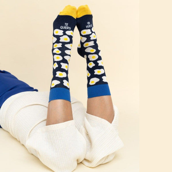 Persona tumbada boca abajo con los pies levantados y los Calcetines con estampado de huevos fritos y el mensaje Te quiero un huevo