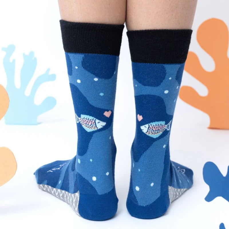 Tobillos con los calcetines con estampado de mar azul y el mensaje "Te quiero mucho / Como la trucha al trucho" rodeados de corales de cartulina