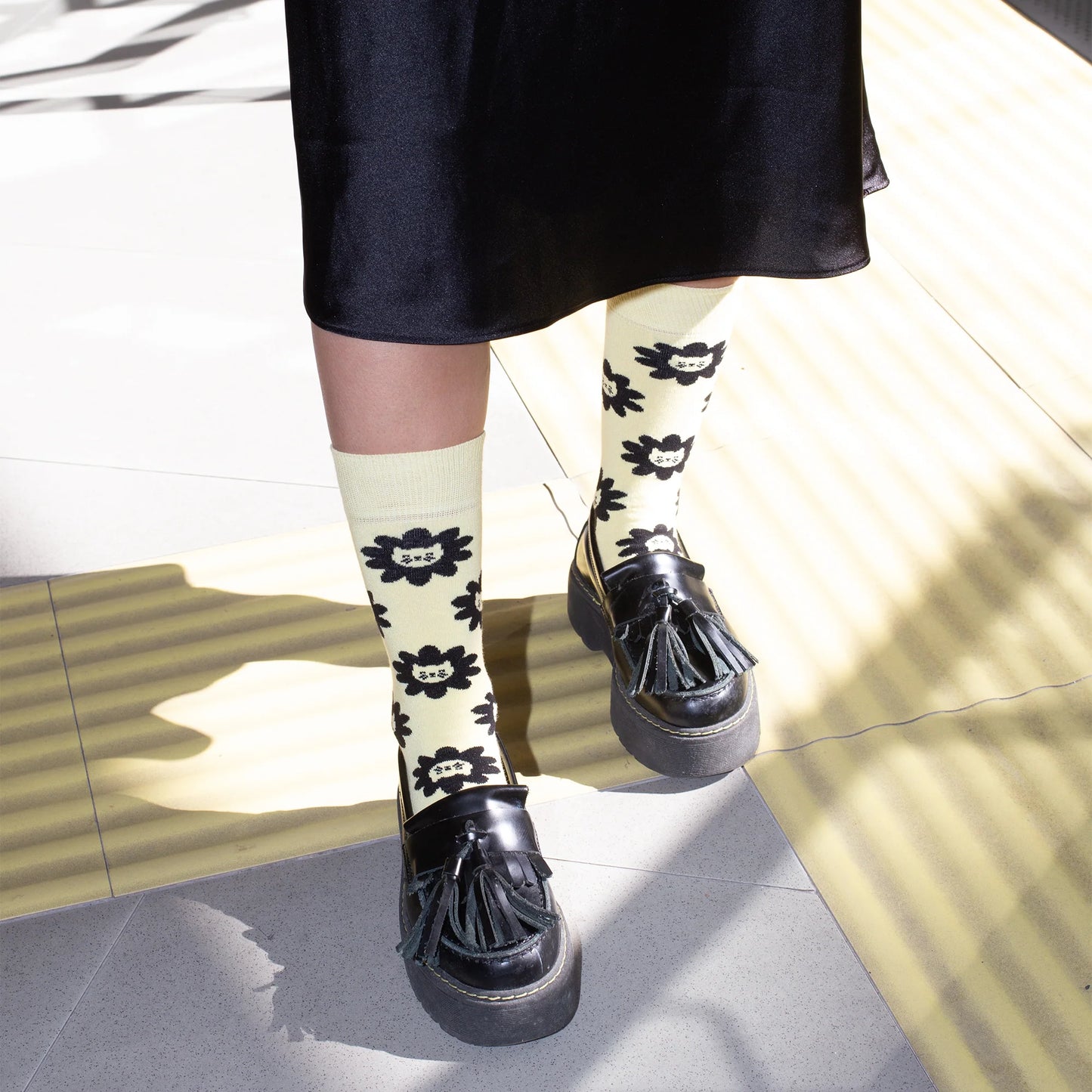 Persona con falda y zapatos castellanos con plataforma y los Calcetines amarillos con estampado de caras de gato y el mensaje "Mi gato manda / yo obedezco"