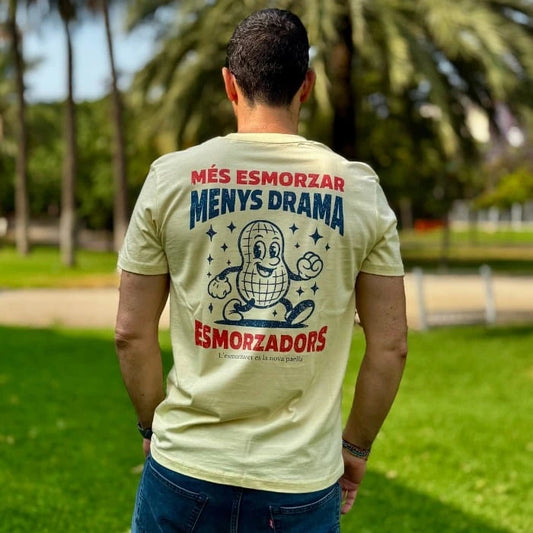 Hombre de espaldas con camiseta de manga corta en la que sale un cacahuete andando y el mensaje "Més esmorzar menys drama"