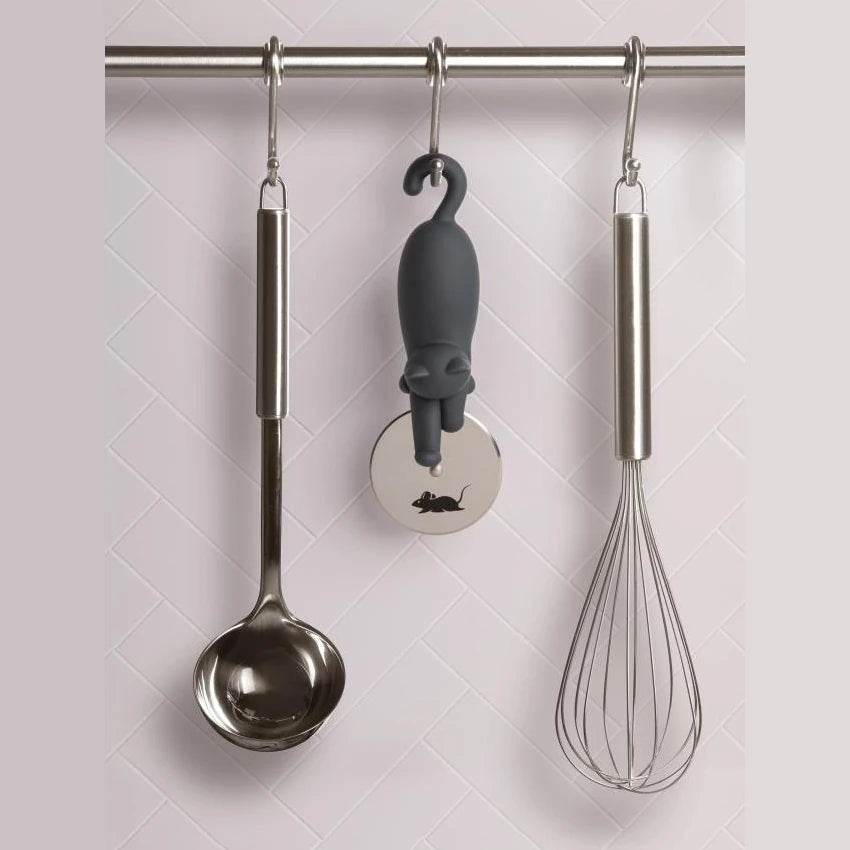 Utensilios de cocina colgados de una barra metálica con ganchos: un cazo, unas varillas y un cortapizzas con forma de gato