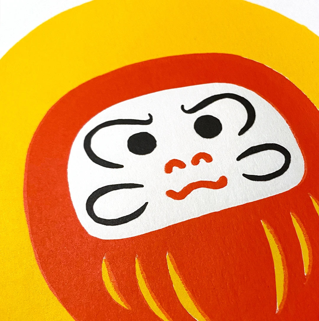 Detalle de Daruma rojo sobre fondo amarillo.