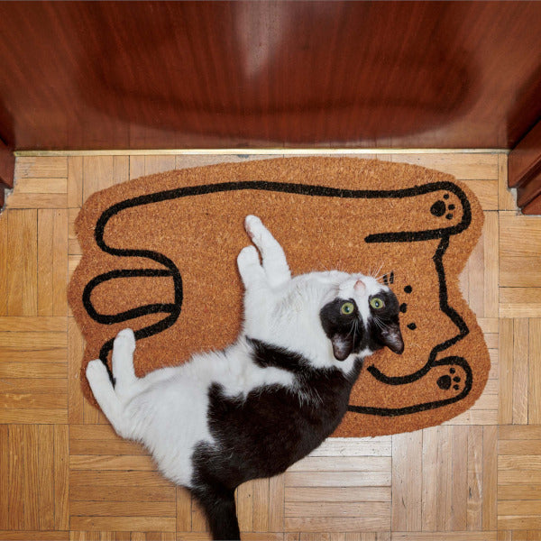 Gato blanco y negro tumbado sobre un felpudo con forma de gato boca arriba