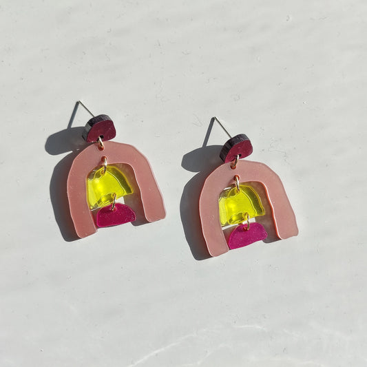 Pendientes de cuatro figuras; la superior de color morado, abajo la mayor que simula una cueva de color rosa y dentro un colgante de una pieza amarilla y otra rosa