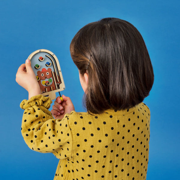 Niña con el juego para niños pinball de madera con cinco bolitas de metal y fondo de oso pardo