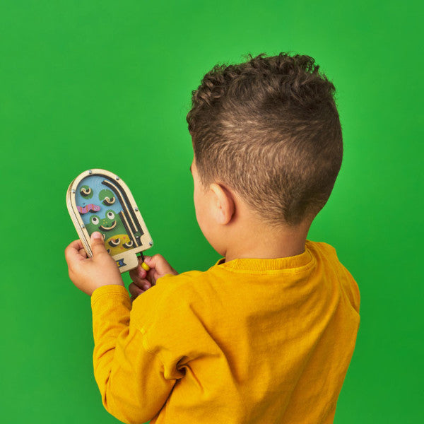 Niño con el juego para niños pinball de madera con cinco bolitas de metal y fondo de rana