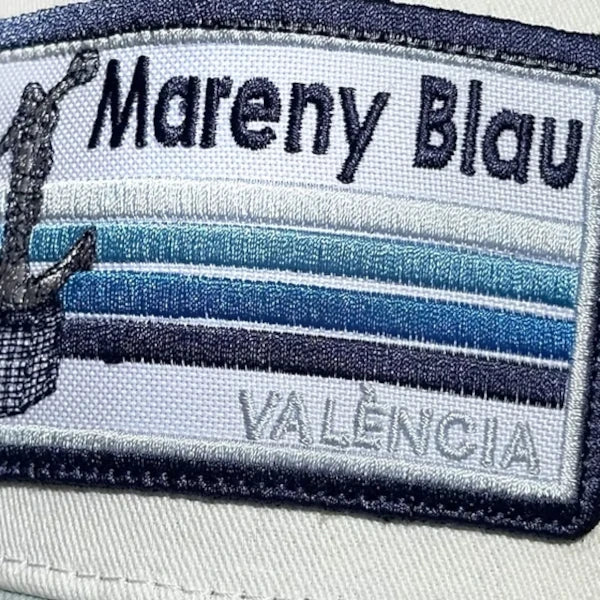 Detalle de la gorra blanca con visera en azul claro con parche de la playa de Mareny Blau, en Valencia