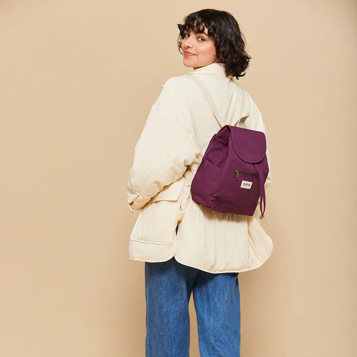 Chica vestida con chaqueta de invierno y vaqueros y la Mochila de tela fuerte pequeña color ciruela de la marca francesa Hindbag