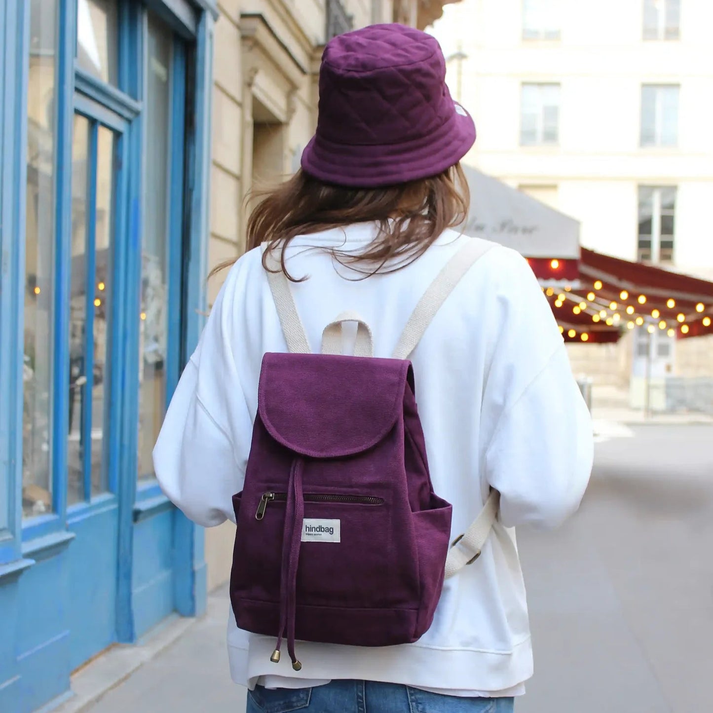 Chica de espaldas con la mochila de tela fuerte pequeña color ciruela de la marca francesa Hindbag y un gorro del mismo color