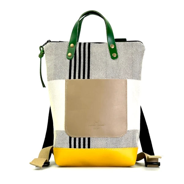 Mochila pequeña reciclada de Daniel Chong con cuerpo de retales de tela en tonos hueso y grises, bolsillo de piel en color beige y bajo en amarillo