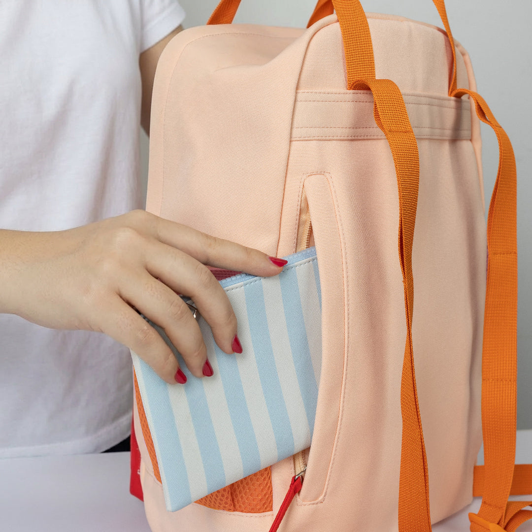 Mujer guardando la cartera en el bolsillo con cremallera trasero de la mochila naranja pequeña con bolsillo y la frase "No me da la vida" bordada