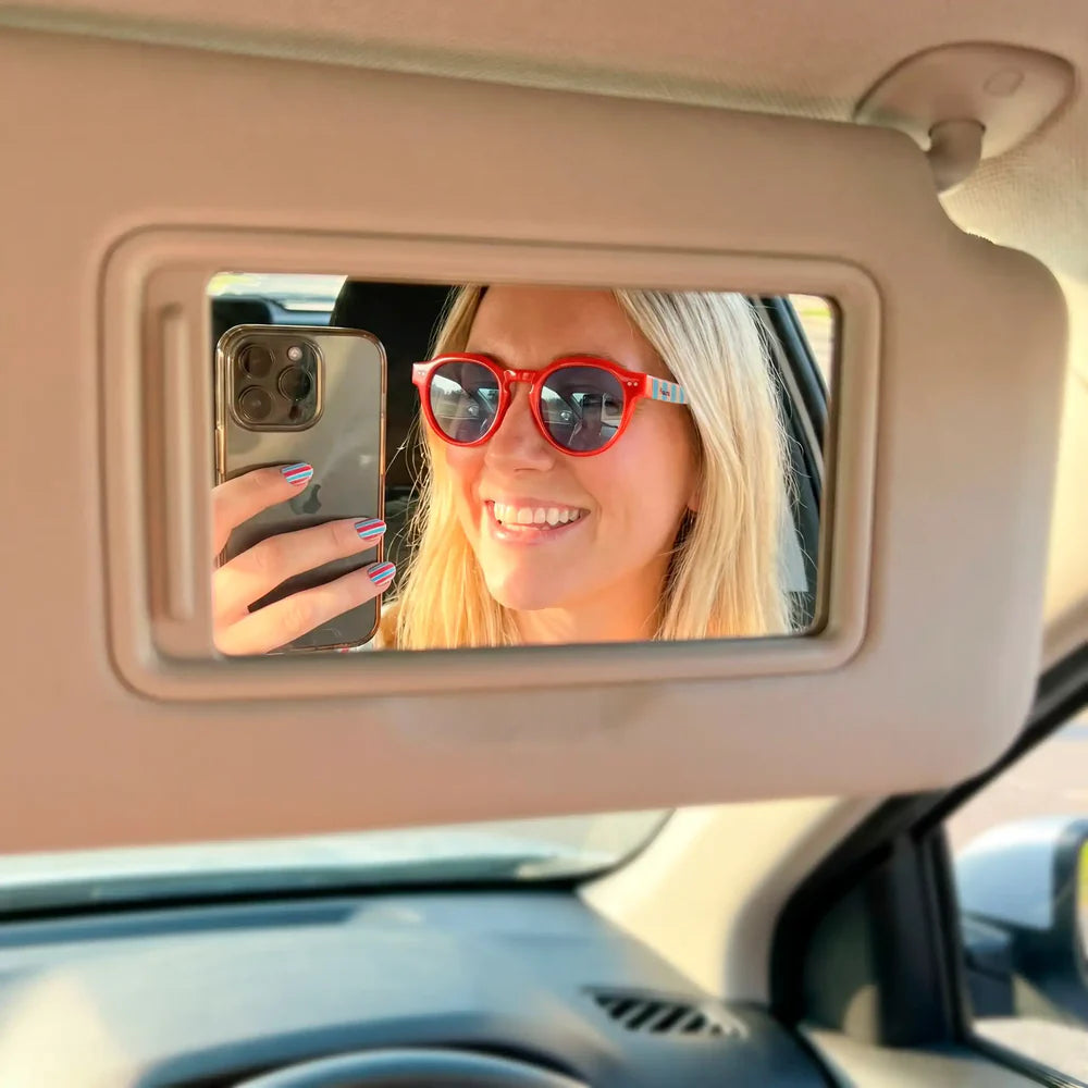 modelo posando con las gafas de sol de Fisura del modelo Out of the office redondas con la parte delantera roja y las patillas a rayas azules y marrones en un coche haciendo un selfie