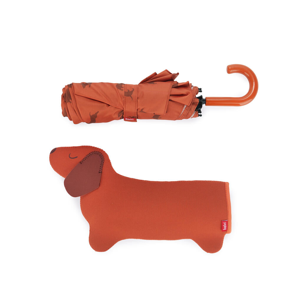Paraguas plegado con estampado de perros salchicha y mango curvo, junto a su funda marrón con forma de perro.