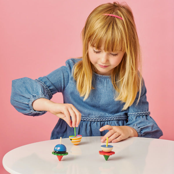 Niña jugando con tres peonzas de madera sobre una mesa blanca