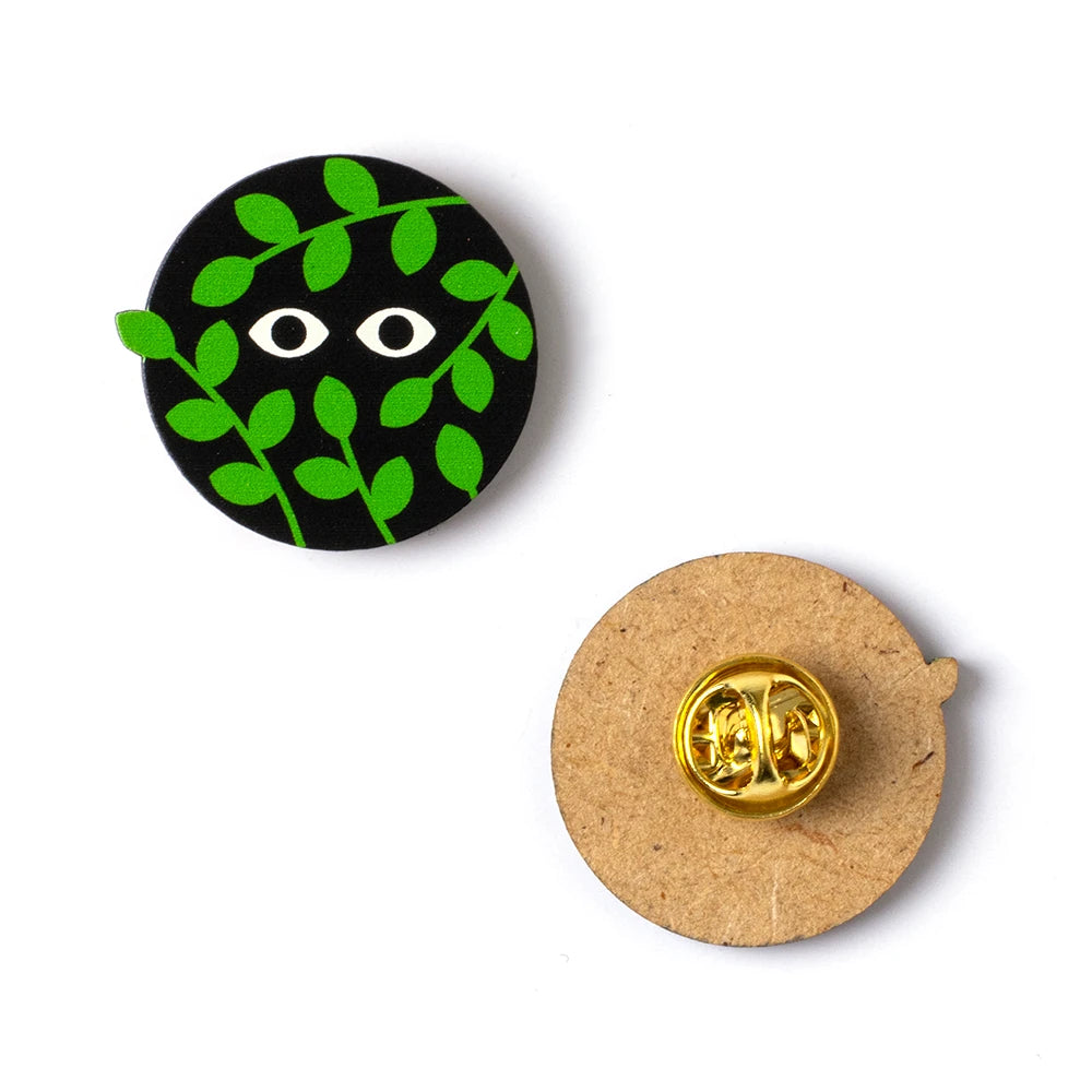 Pin de madera redondo con forma de ojos que miran desde detrás de las hojas por delante y por detrás
