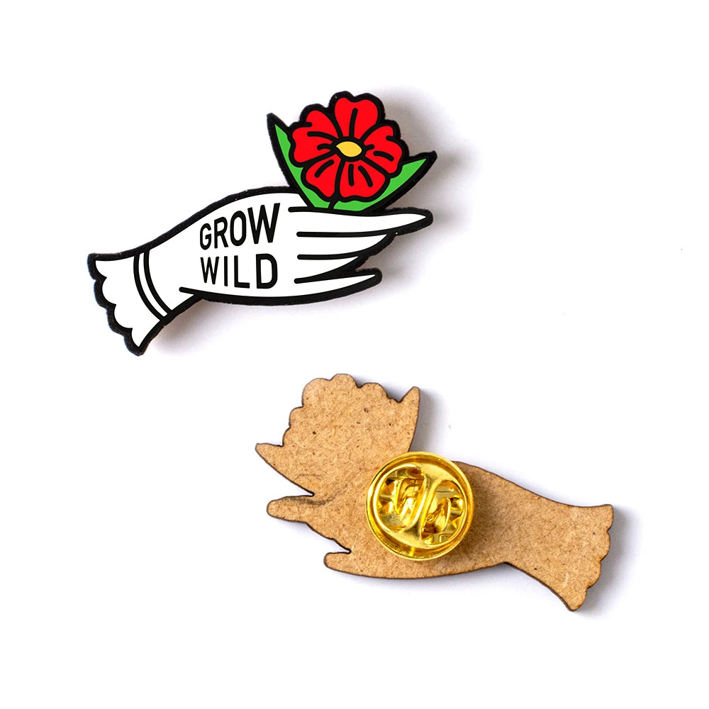 Pin de madera con forma de mano con guante blanco sosteniendo una flor roja con el mensaje Grow wild