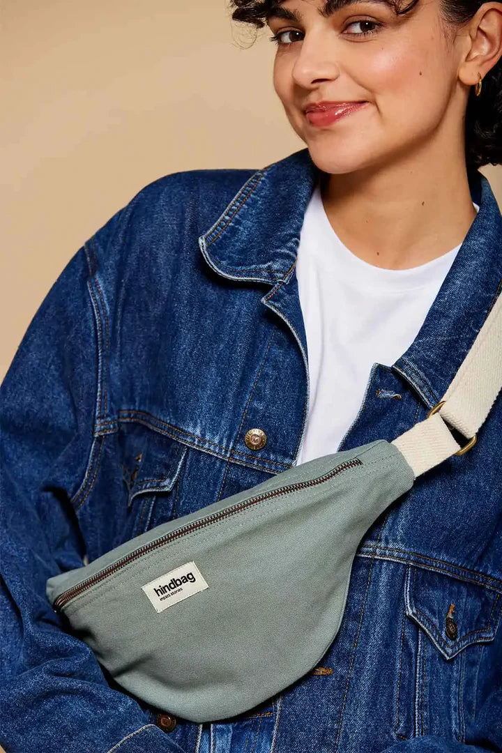 Mujer con chaqueta vaquera y riñonera de la marca francesa Hindbag color azul verdoso salvia y correa blanca