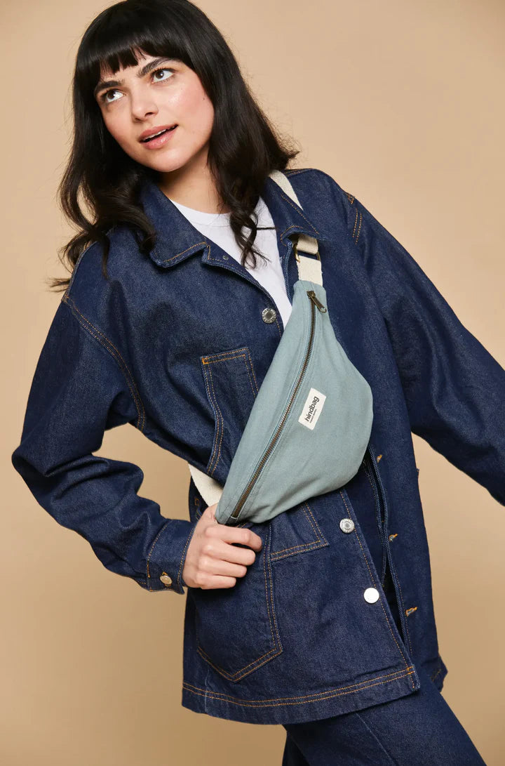 Mujer con camisa vaquera y riñonera de la marca francesa Hindbag color azul verdoso salvia y correa blanca