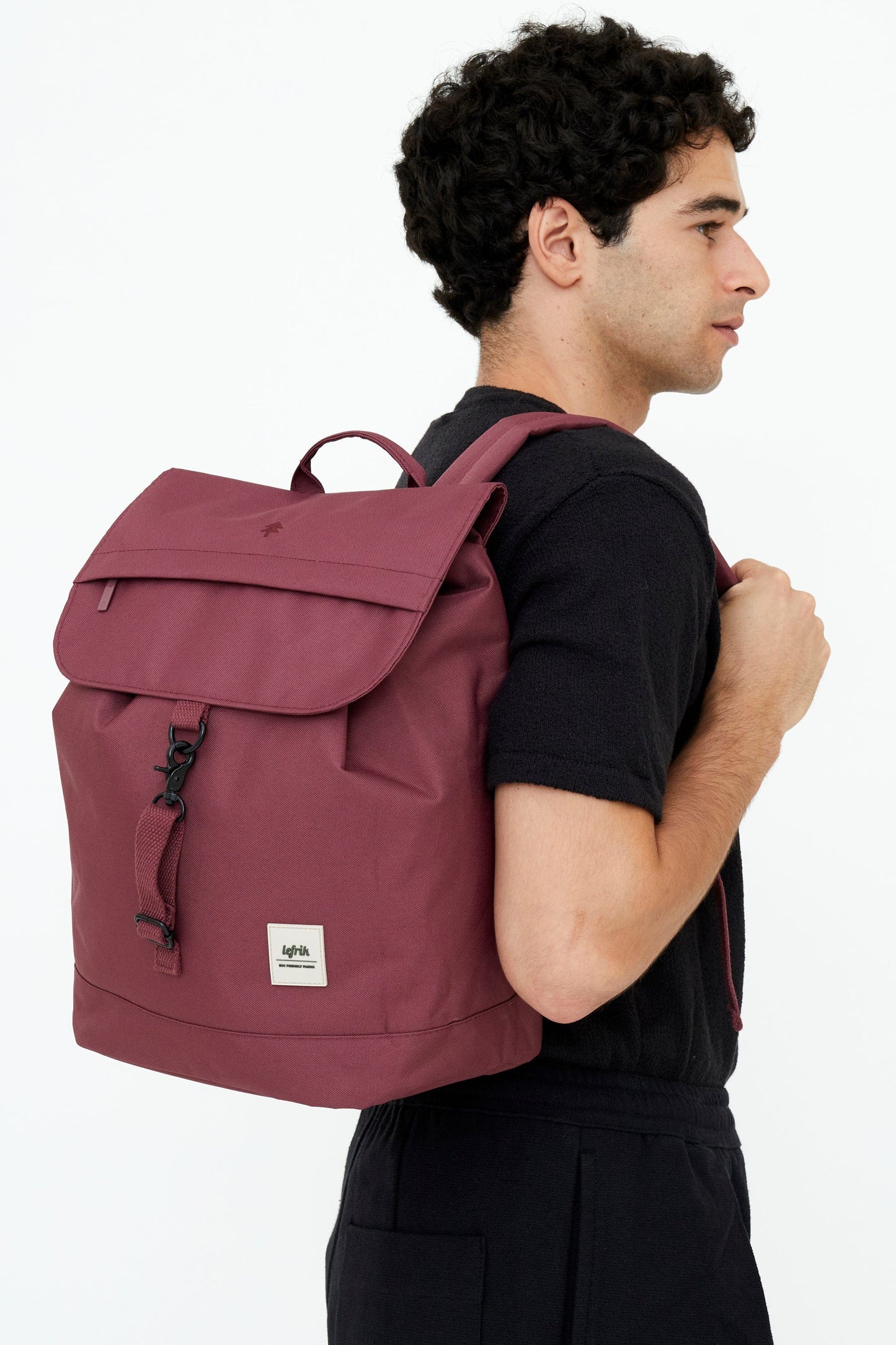 Chico vestido de negro con una mochila grande color ciruela al hombro