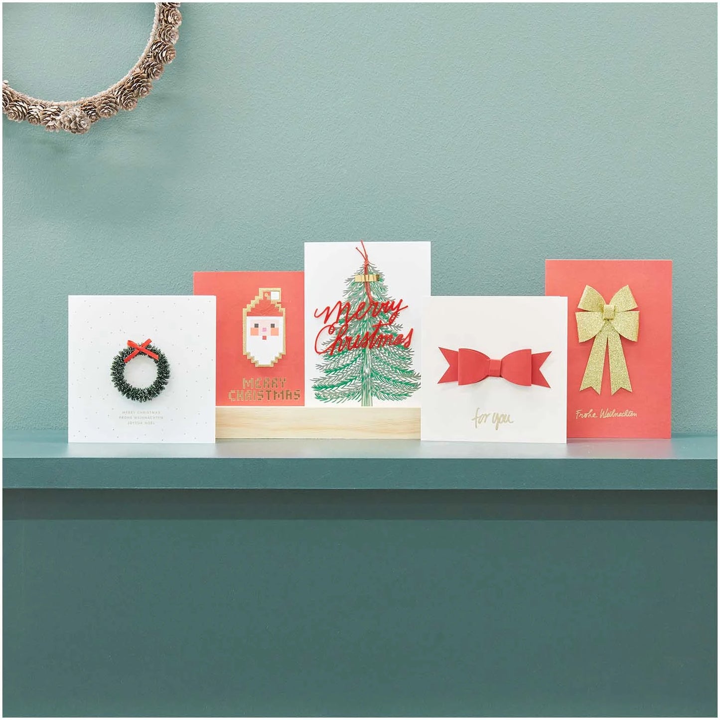 conjunto de cinco postales con textos navideños y diferentes motivos navideños, como un papá Noel pixelado, un árbol de navidad con el texto "merry christmas", dos postales con un lazo simulando un regalo con el texto "for you" y un adorno de puerta navideño con hojas de pino y el texto "feliz navidad" en inglés, francés y alemán