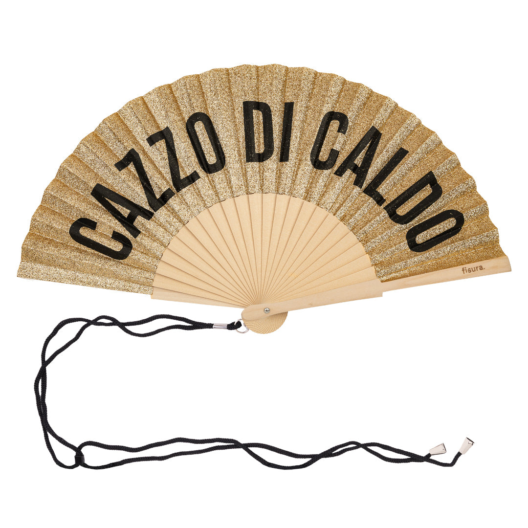 abanico de la marca fisura de tela y madera en color purpurina dorada con el texto CAZZO DI CALDO en negro, con una cuerda negra enganchada para colgarlo a la muñeca o al cuello