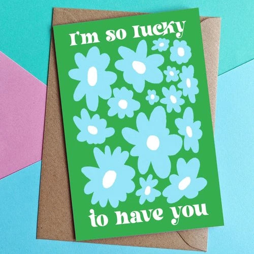 tarjeta de la ilustradora Laura Ortiz con el texto I'm so lucky to have you, con flores azules y sobre fondo verde