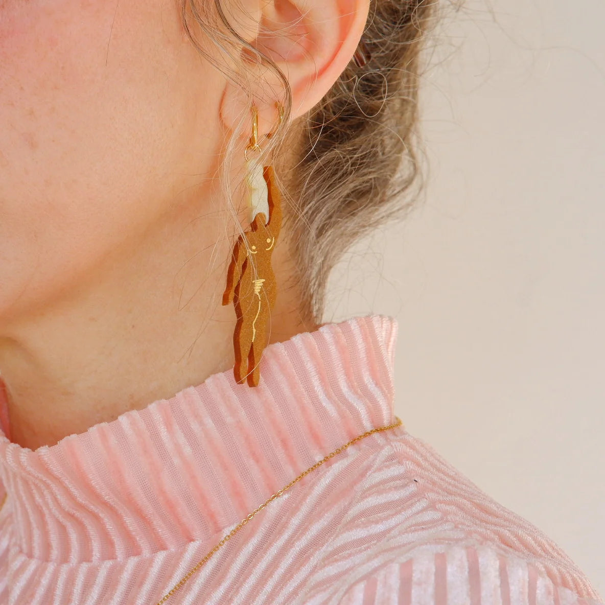 mujer llevando puestos los pendientes de metacrilato con aro dorado de la artista mitumi con dos mujeres nadando desnudas en color marrón con el pelo rubio