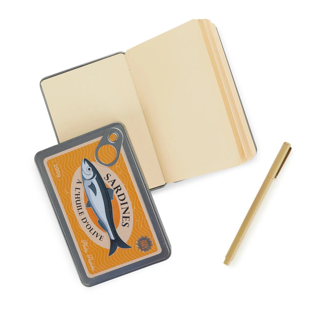 libreta en forma de lata de conservas en color amarillo y con partes metálicas y una sardina en el centro con el texto Sardines a l'huile d'olive y la libreta abierta al lado con las páginas tintadas de amarillo , y un boli