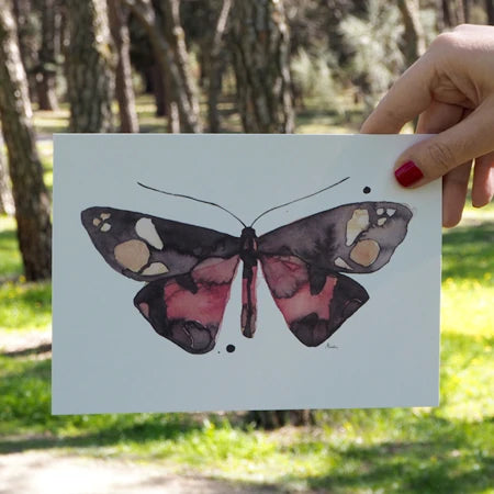 mano de una persona con las uñas pintadas de rojo sujetando la lámina de Marialu de una mariposa Leteo borealis hecha con acuarelas