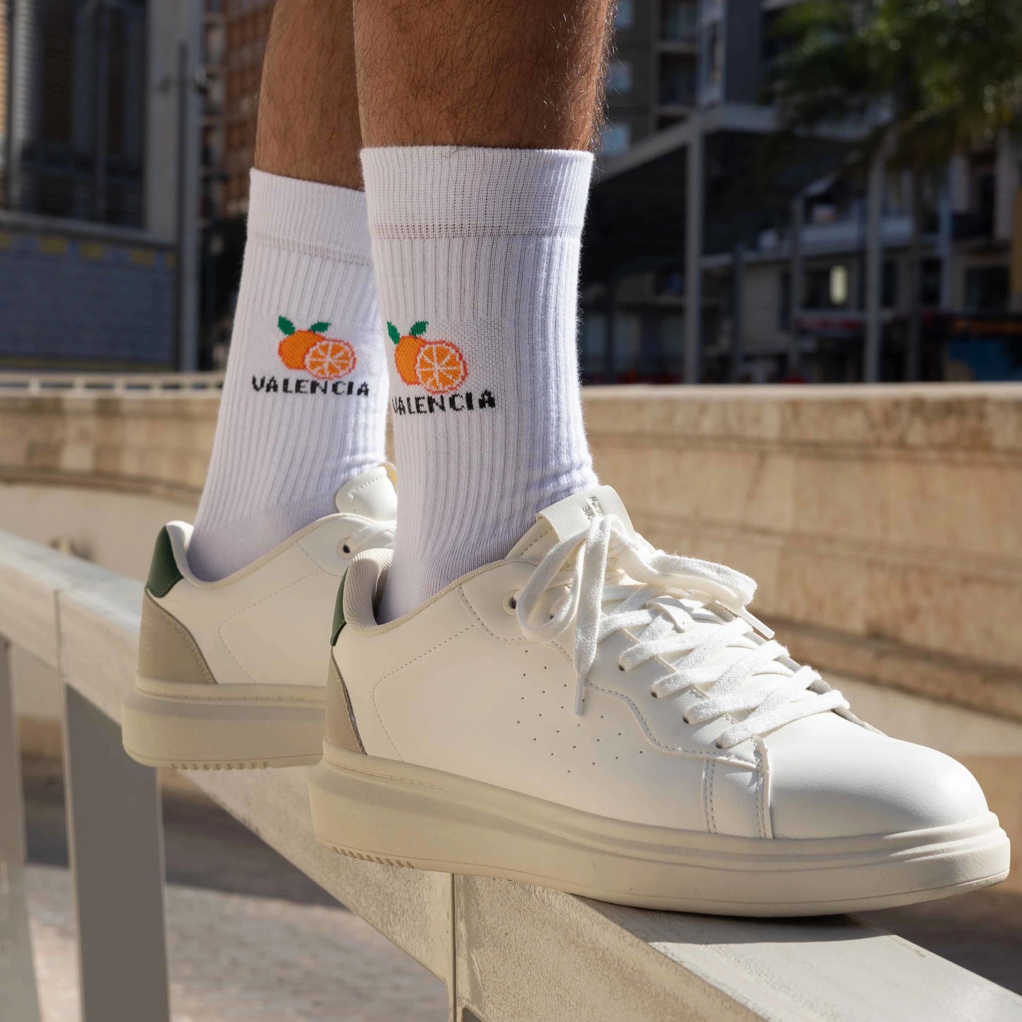 Pies de hombre con zapatillas deportivas blancas y calcetines blancos con detalle de naranjas y la palabra Valencia