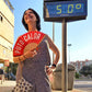 Mujer abanicándose en Sevilla bajo un termómetro que indica 50 grados con un abanico rojo en el que pone Puto Calor